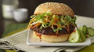 burger on seeded bun with lettuce and shaved carrots, cucumbers on the site