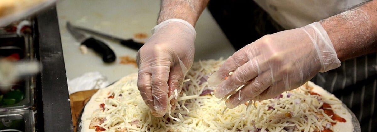 Gloved hands making pizza