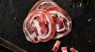 Sliced and diced pancetta on dark table background with wooden handle knife and scattered cracked black pepper